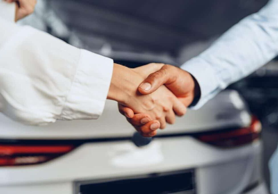 Car seller and buyer handshake at car dealership against a new car